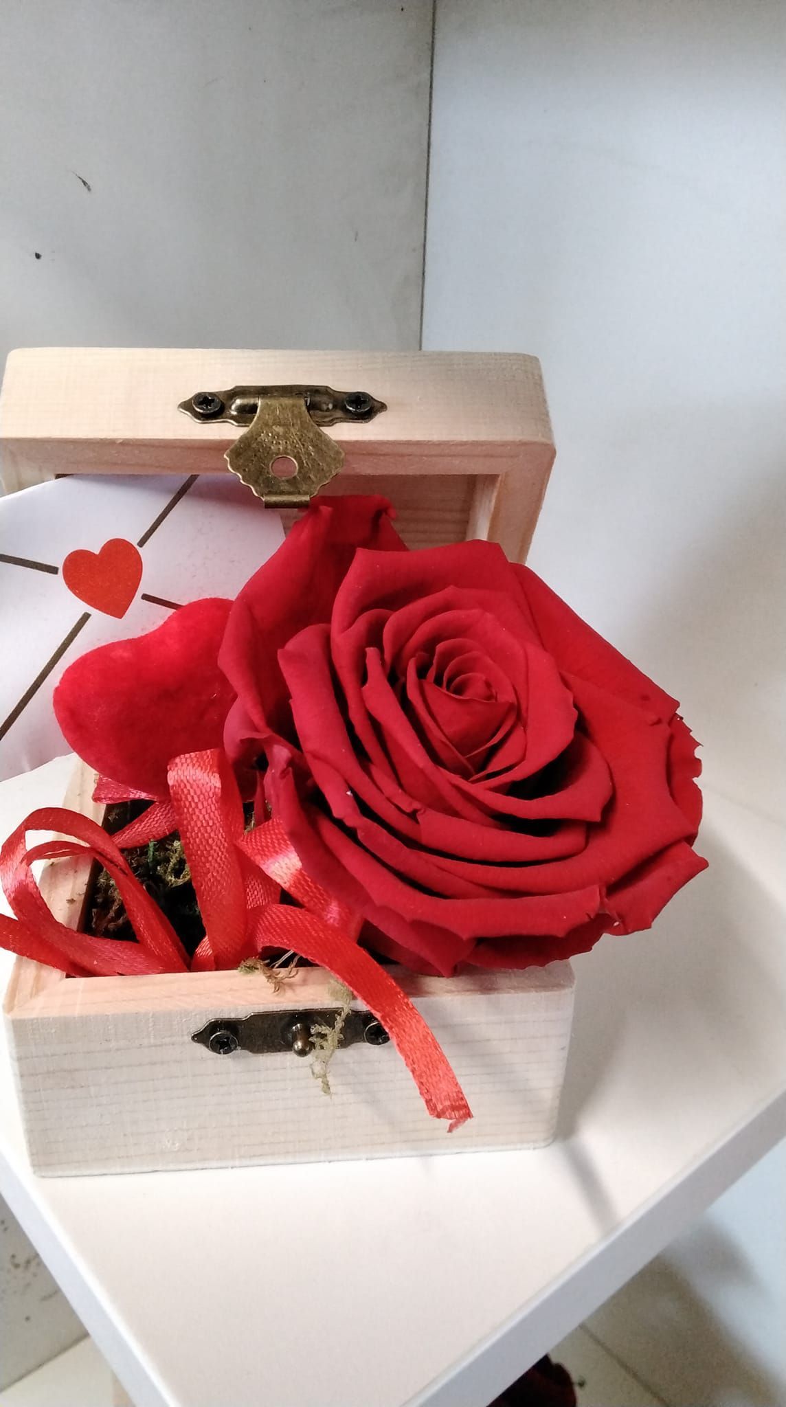 Una rosa rossa è in una scatola di legno su un tavolo.
