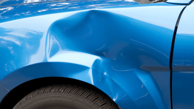 A close up of a blue car with a damaged fender.