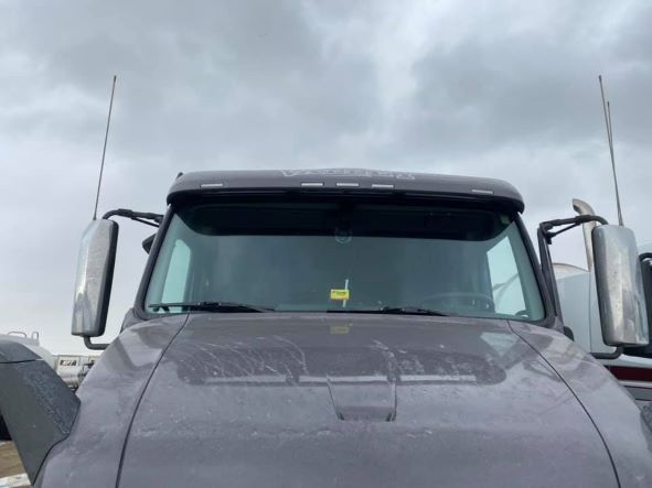 The front of a gray truck with a sun visor on the windshield.