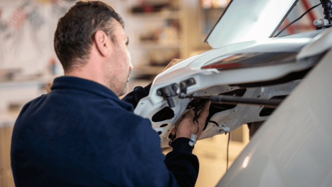 A man is working on the trunk of a car in a garage.