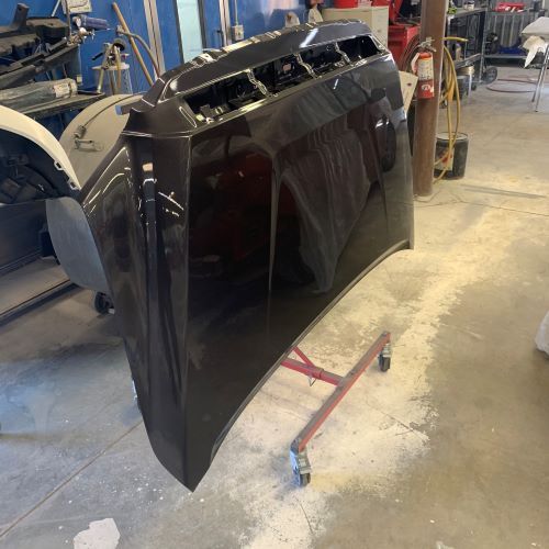 A black car hood is sitting on a red stand in a garage.