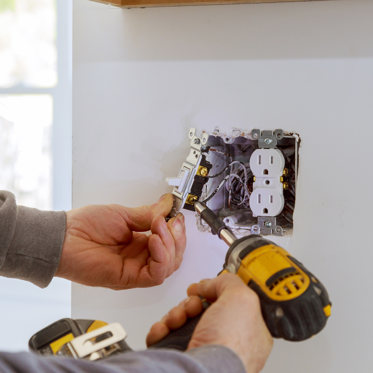 Harrington Electric LLC - A man is installing an electrical outlet with a drill