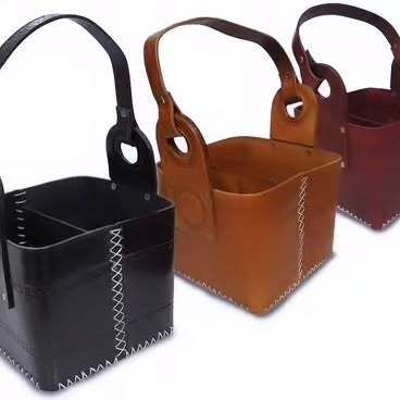 Tres cestas de cuero con asas están colocadas una al lado de la otra sobre una superficie blanca.