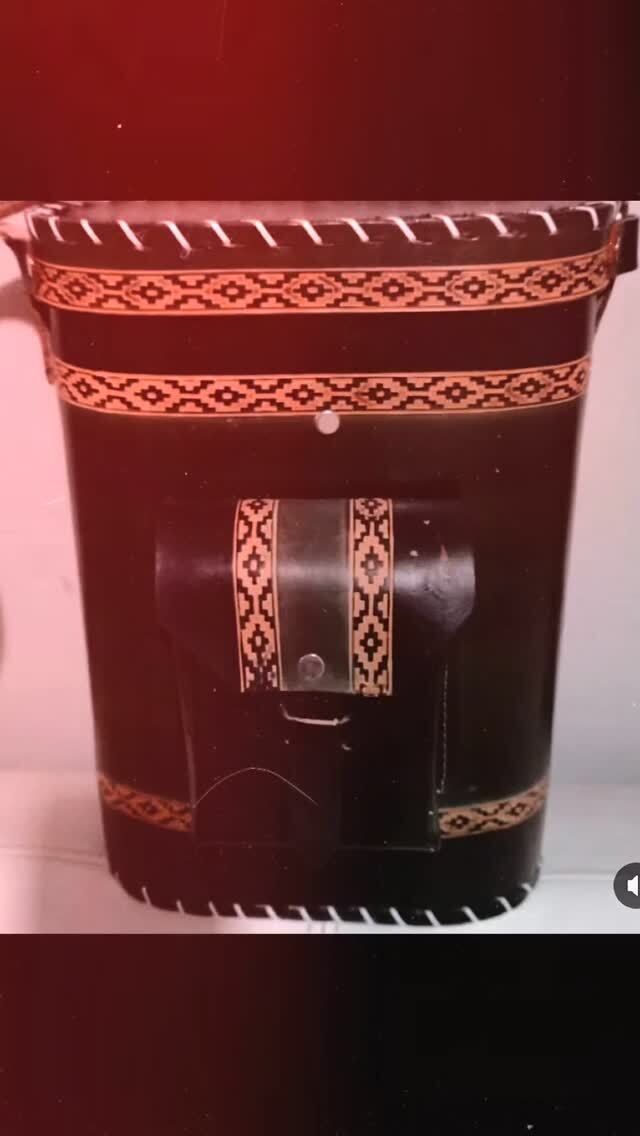 Un bote de basura negro con un borde rojo está sobre un estante.