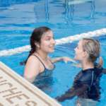 Two women are talking in a swimming pool.