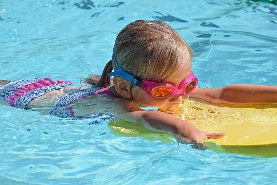 A little girl wearing goggles is swimming in a pool.