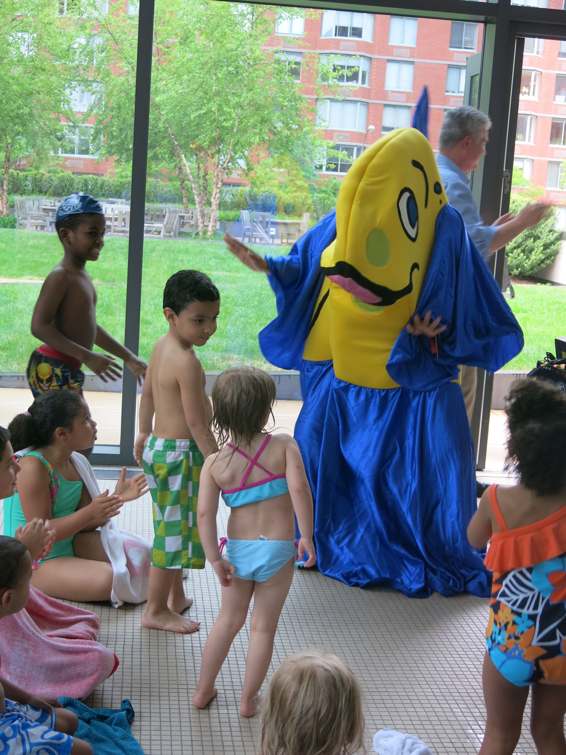 A group of children are standing around a mascot in a blue and yellow outfit