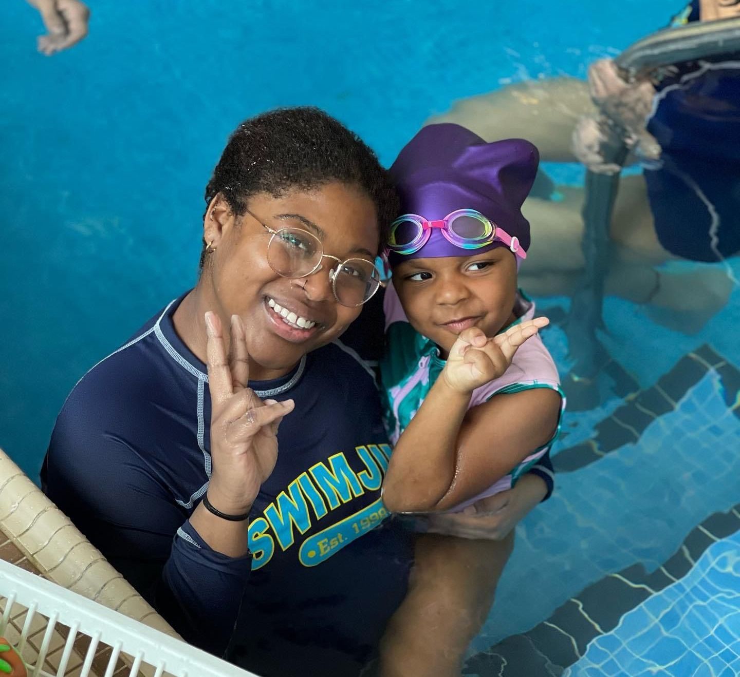 A woman in a swim shirt is holding a child in a pool