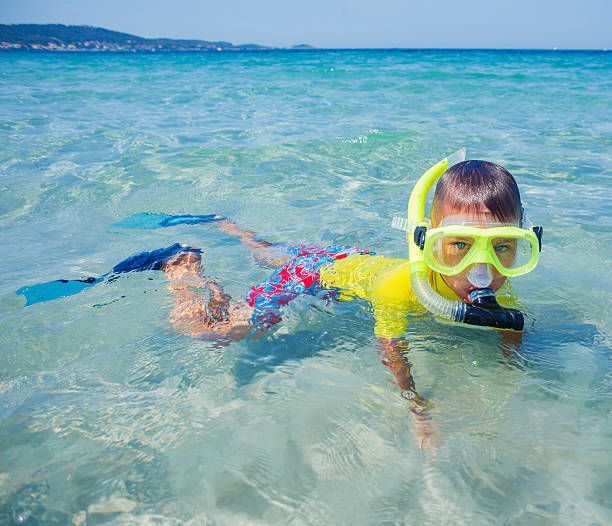 A young boy is swimming in the ocean wearing a mask and flippers.