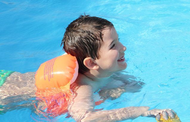 A young boy is swimming in a pool wearing a life preserver.