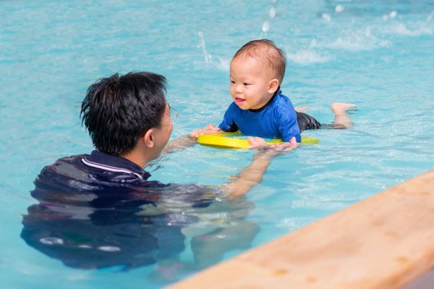 A man is teaching a baby how to swim in a swimming pool.