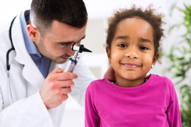 A doctor is examining a little girl 's ear with an otoscope.