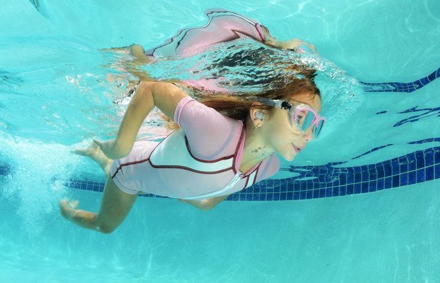 A young girl is swimming underwater in a swimming pool.