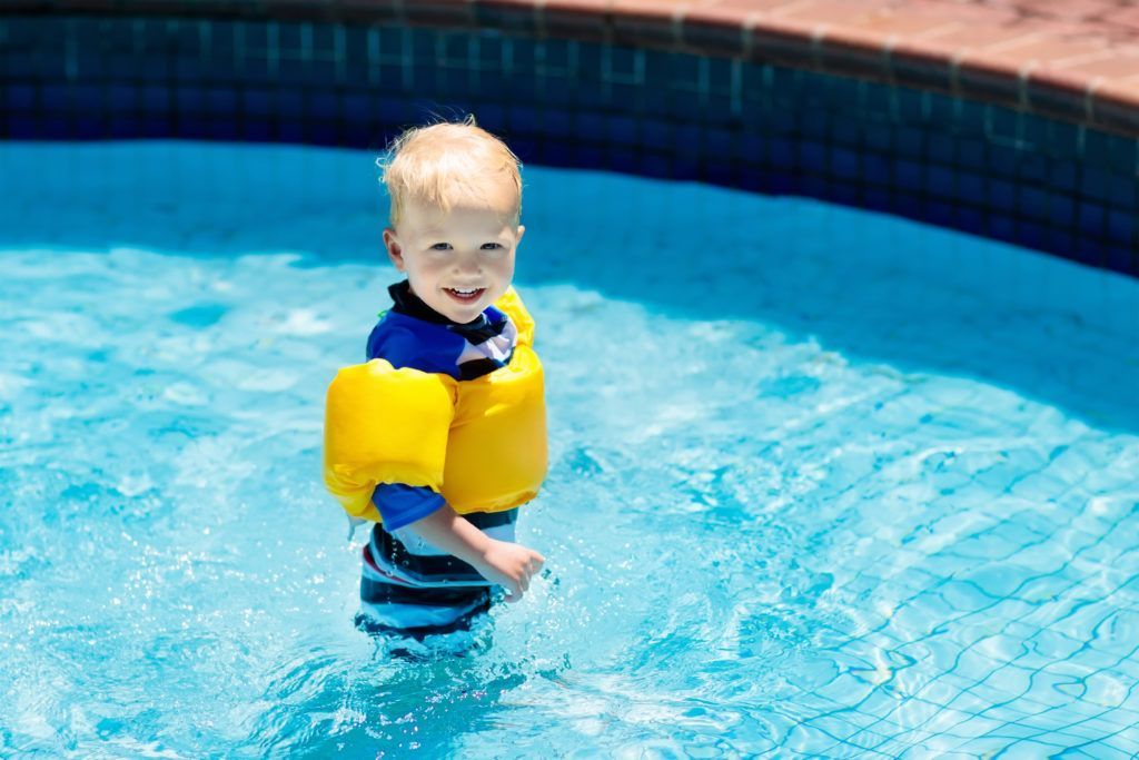 A young boy wearing a life jacket is standing in a swimming pool.