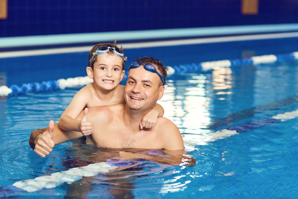 A man and a boy are swimming in a swimming pool.