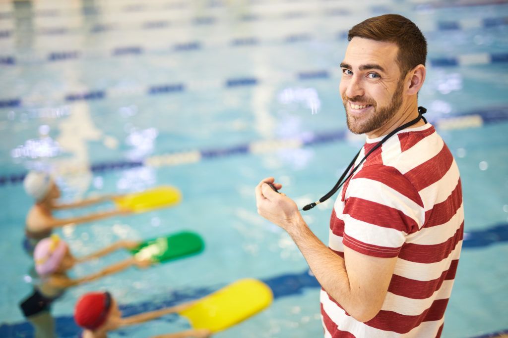 A man is standing in front of a swimming pool with children.