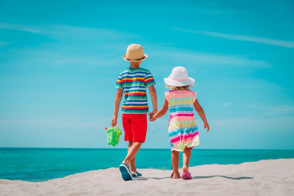 A boy and a girl are walking on the beach holding hands.