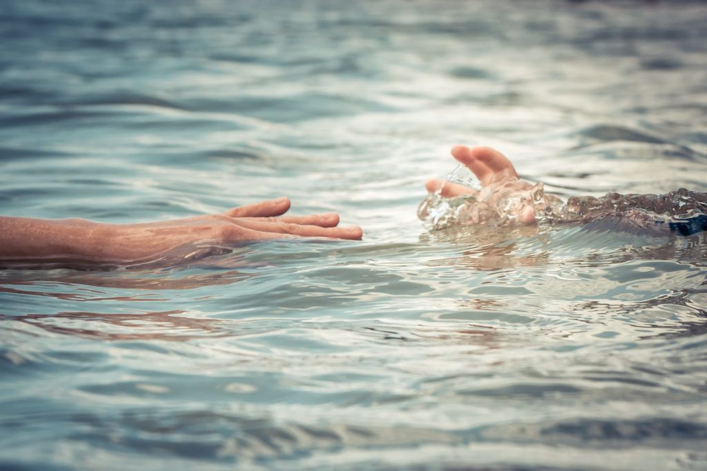 A person is reaching out to help another person in the water.