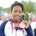 A woman is holding a medal around her neck and smiling.