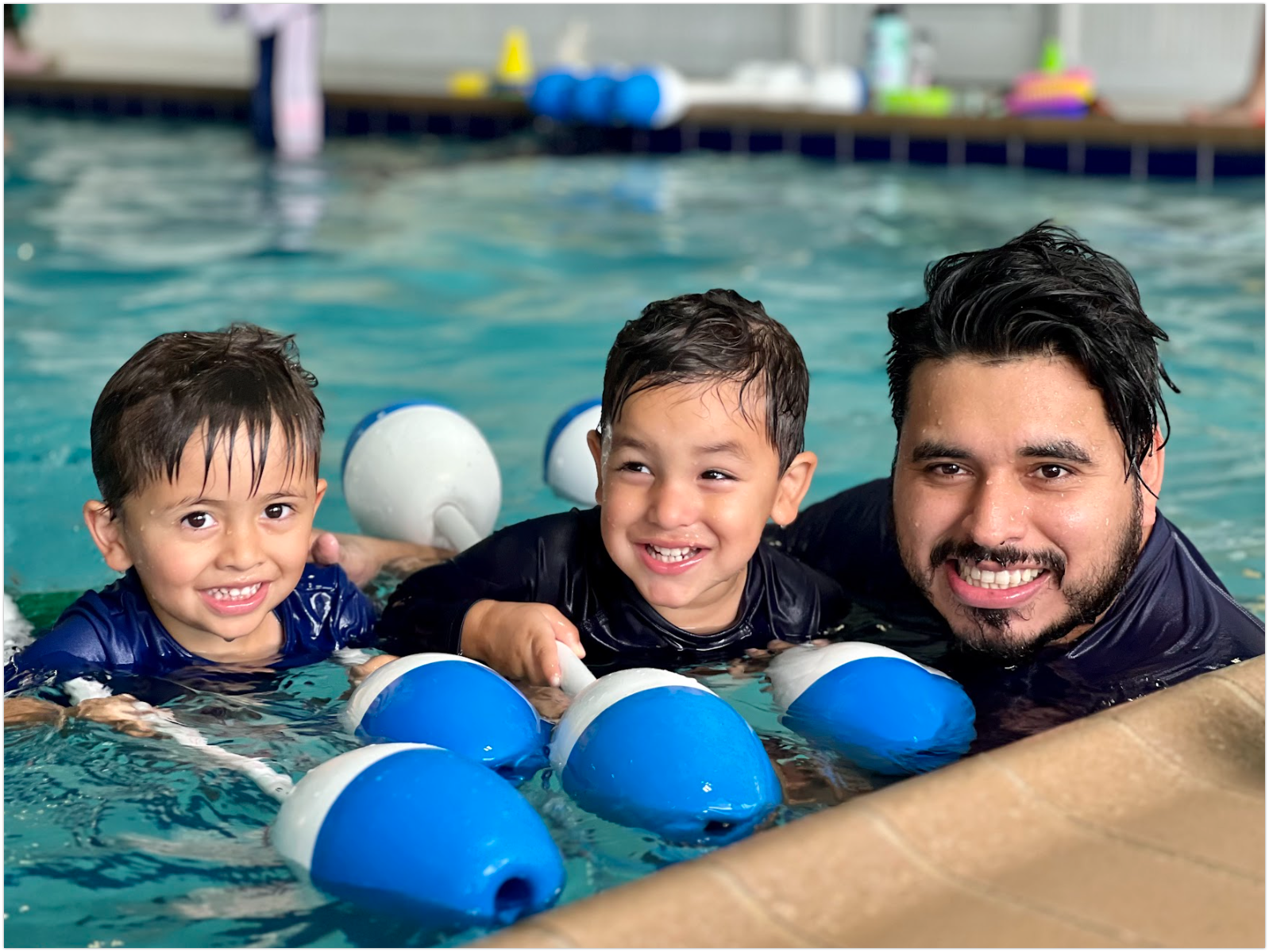 A man is teaching two young boys how to swim in a swimming pool.