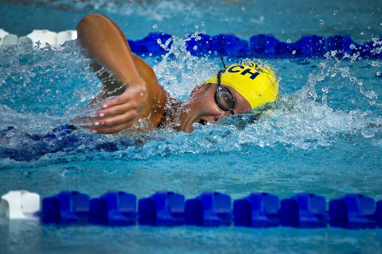 A woman is swimming in a pool wearing a yellow cap that says ch