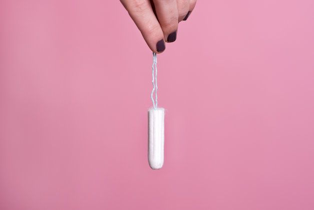 A woman is holding a tampon in her hand on a pink background.