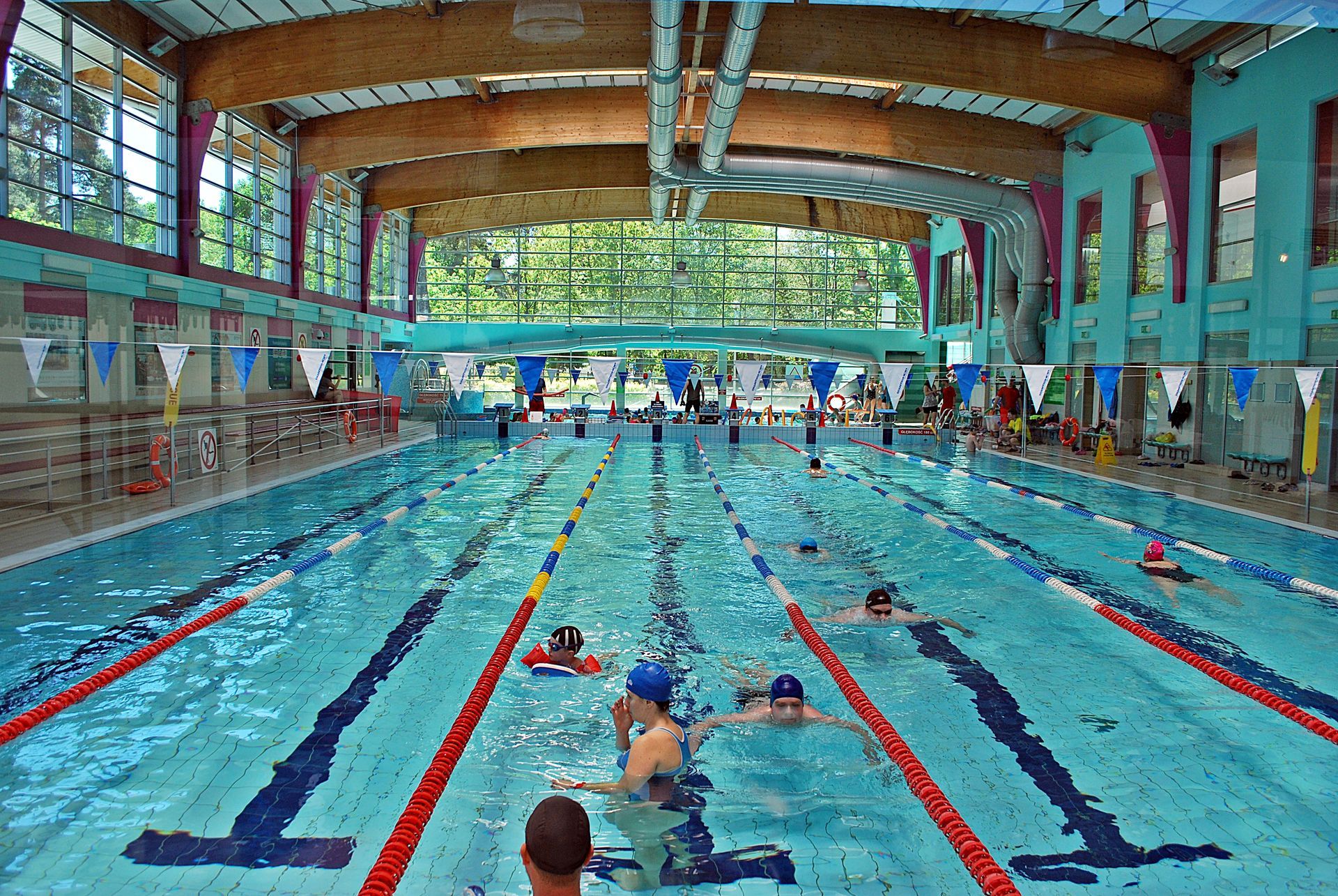 Indoor lap pool with swimmers practicing in marked lanes under bright natural light.