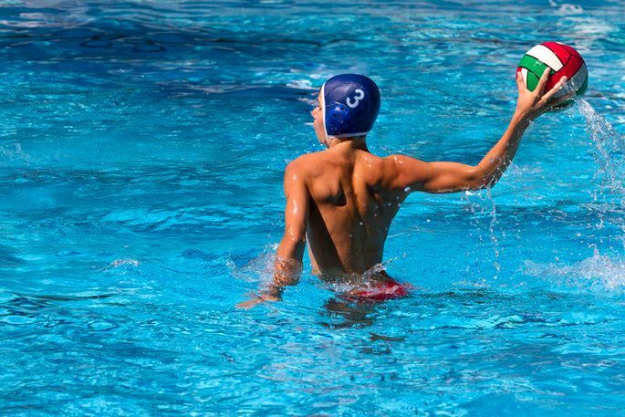 A young boy is playing water polo in a swimming pool.