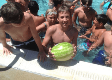 A group of children are playing in a swimming pool and one of them is holding a watermelon.