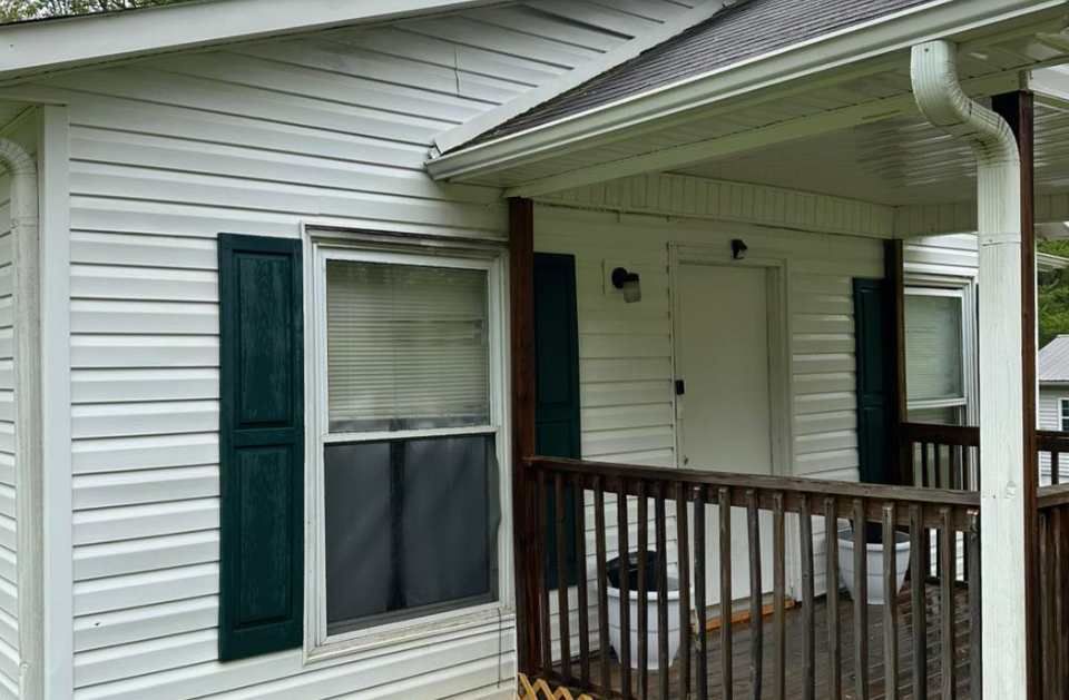 A white house with a porch and a window with green shutters.