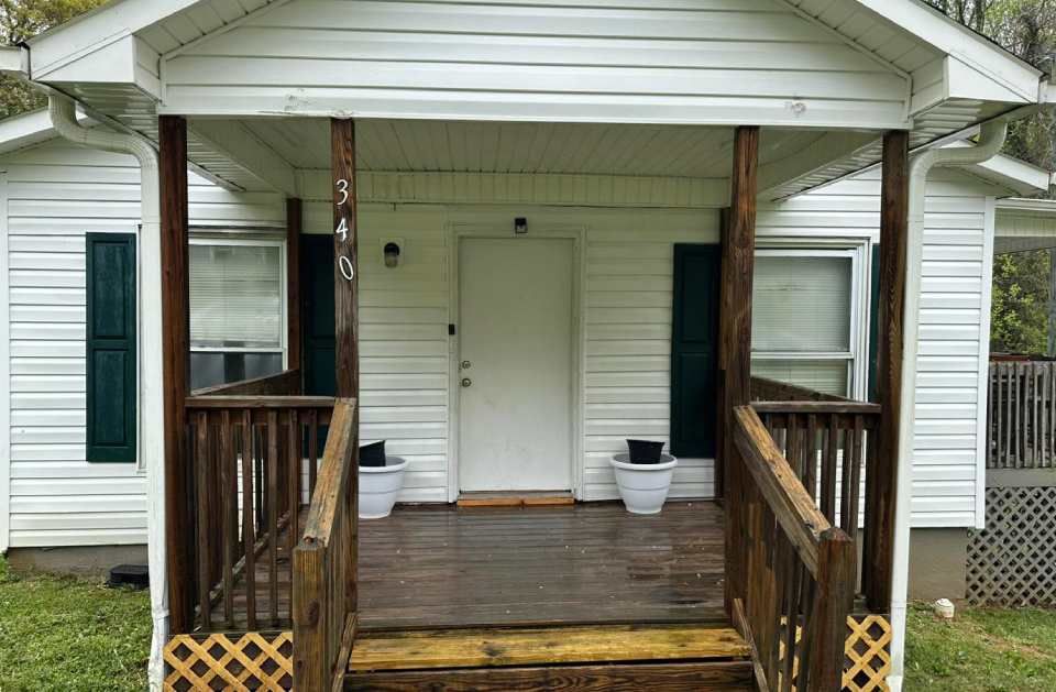 A small white house with a porch and stairs leading up to it.