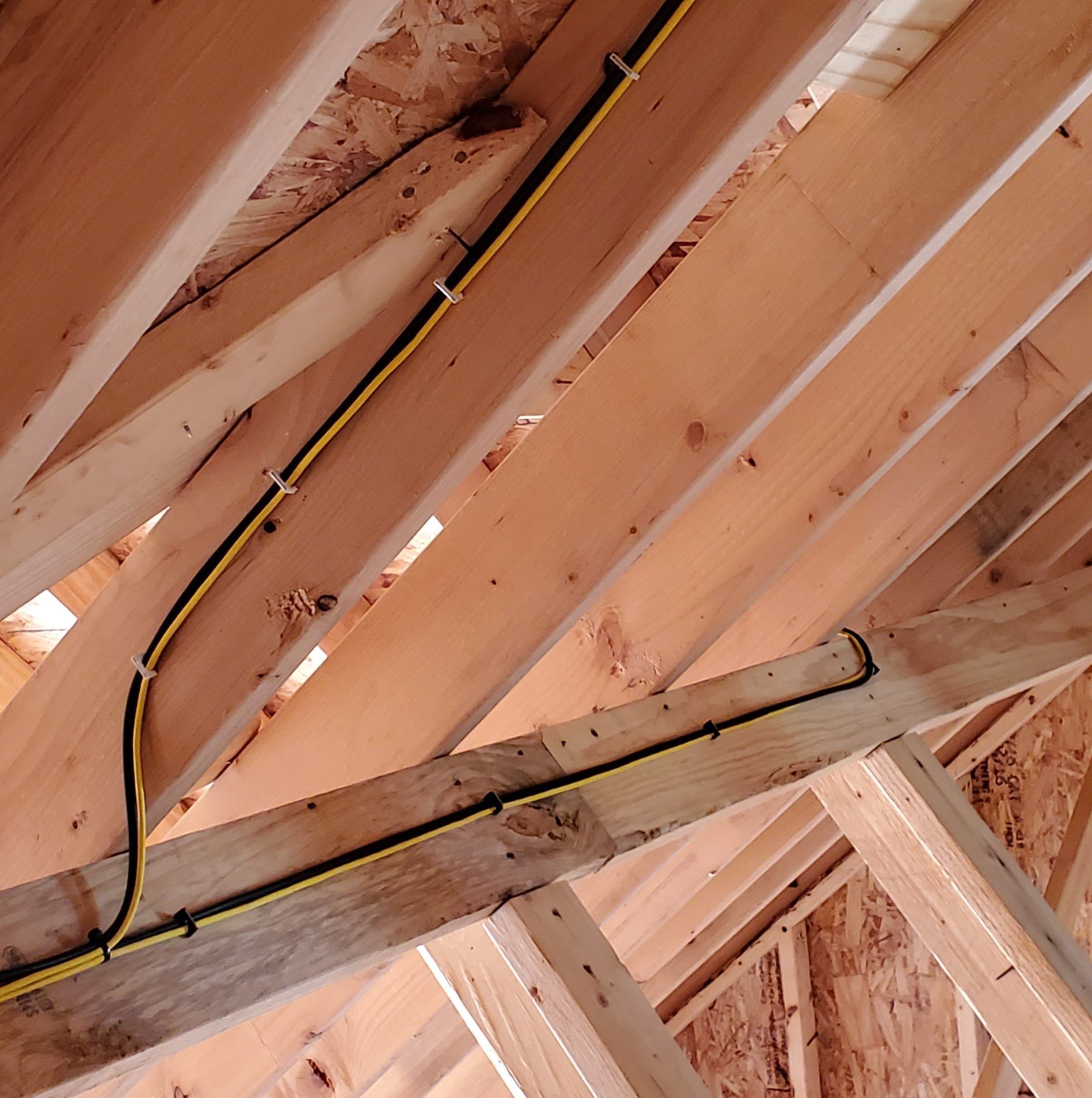 Wooden rafters with electrical wiring secured along the beams.