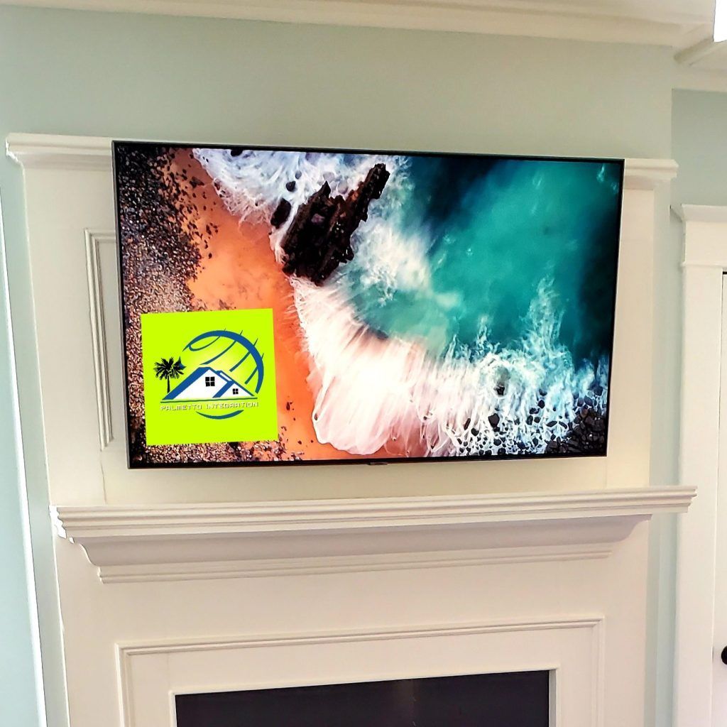 TV mounted above a fireplace, displaying a beach scene; a logo is visible on the screen.