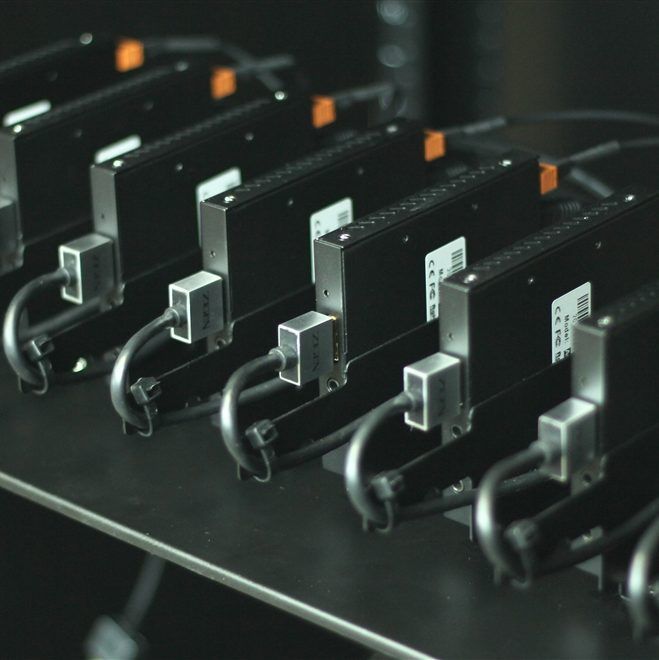 Row of black rectangular electronic devices connected by cables on a metal rack.