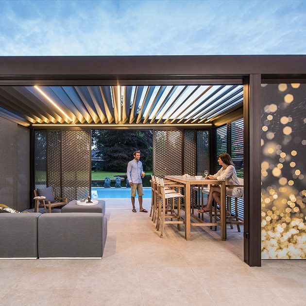 Outdoor patio with seating, dining area, and pool view; people stand and sit under a pergola.