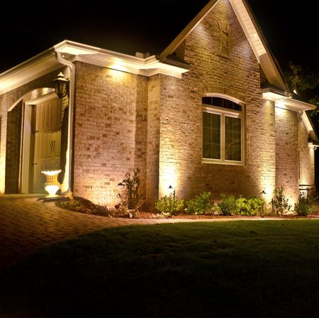 Garage exterior at night with brick arches, wood doors, and ambient lighting. A brick paver driveway leads up to the garage.