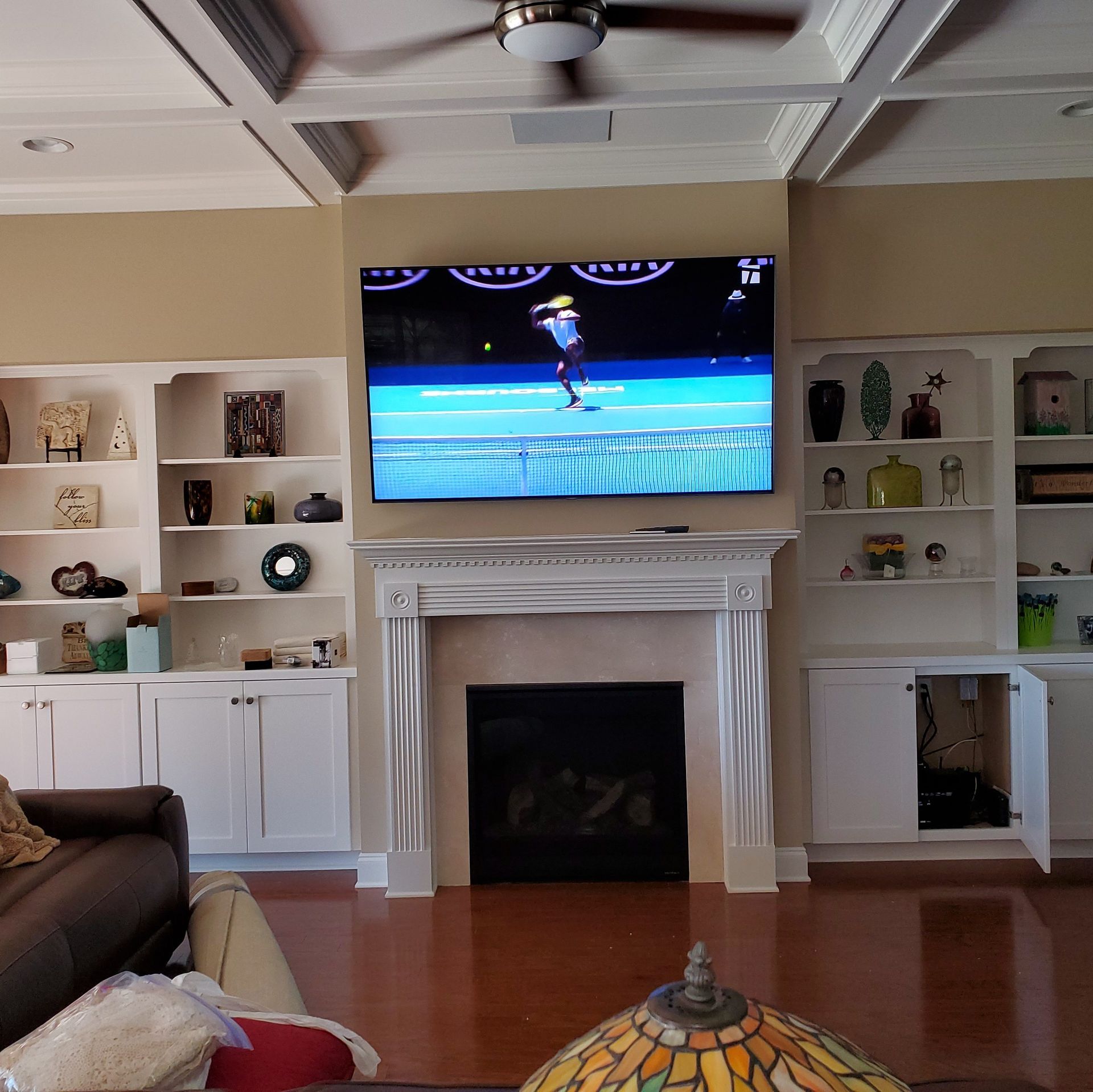 Living room with a fireplace, built-in bookshelves, and a TV playing a tennis match.