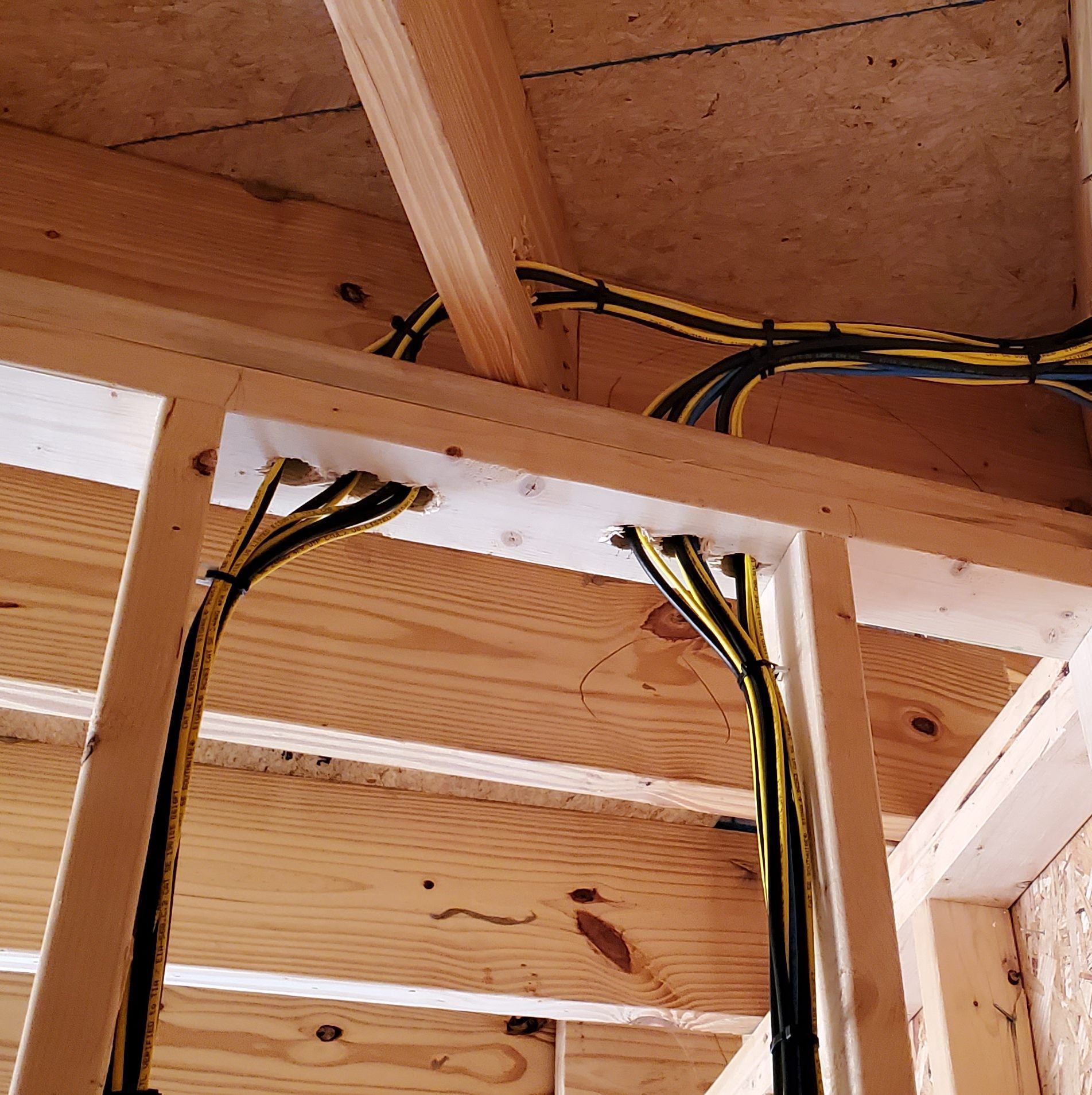 Electrical wiring routed through wooden framing in a construction site. Black and yellow cables are secured with clips.