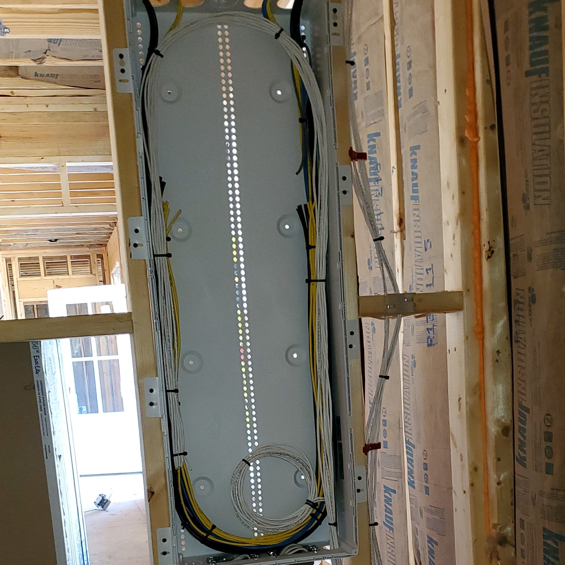 White rectangular cable tray installed between wooden beams, holding bundles of wires. Interior construction setting.