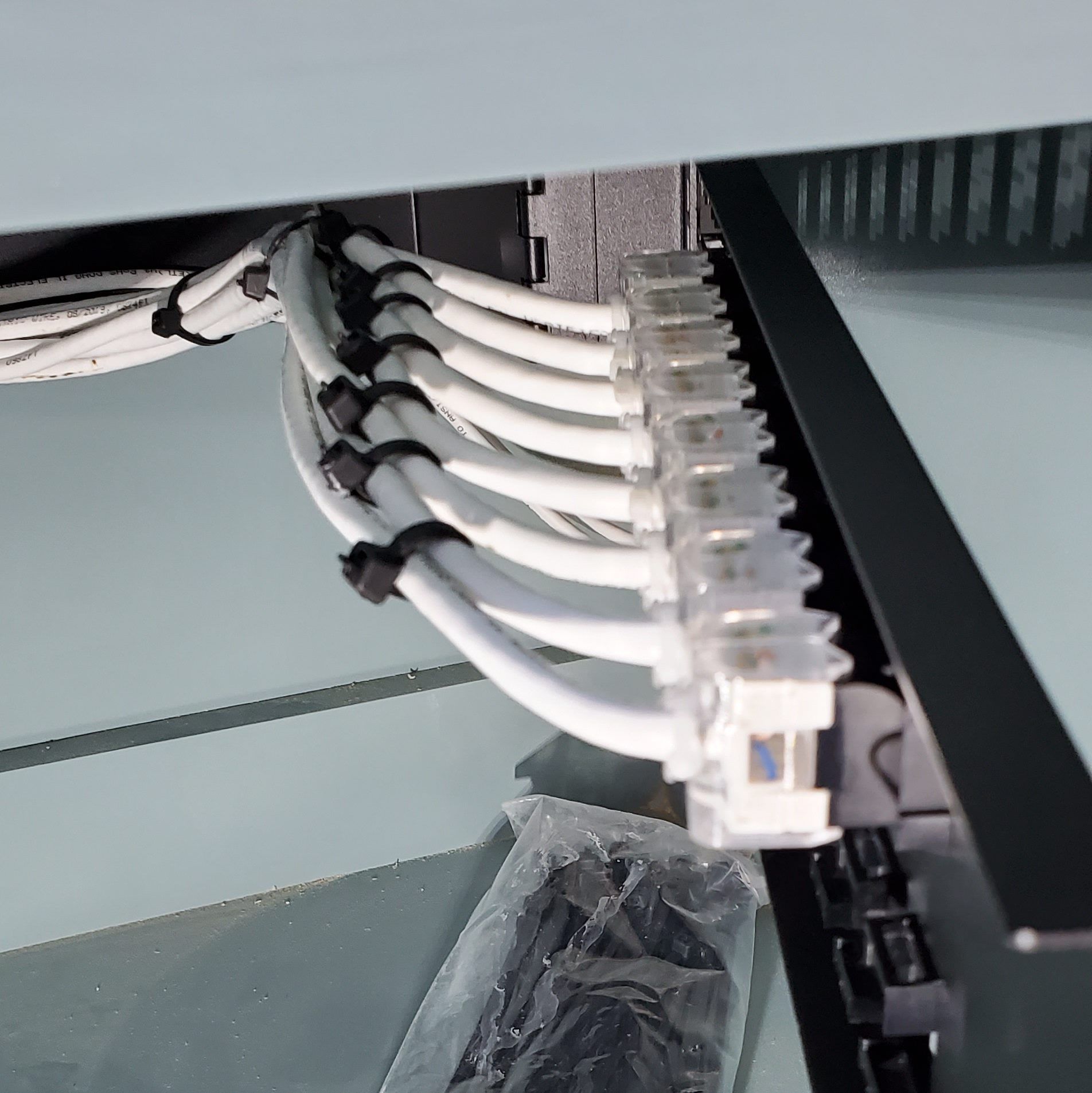 Network cables connected to a patch panel inside a rack. White cables with clear connectors, secured with cable ties.