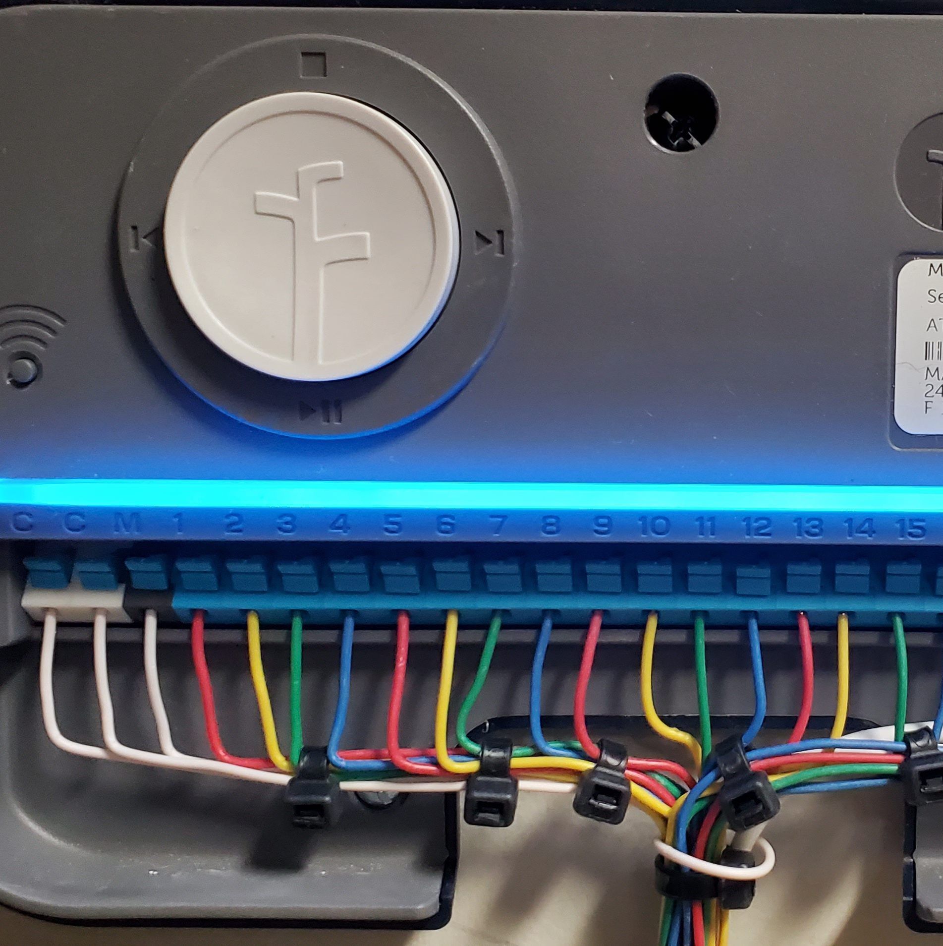 Close-up of a sprinkler system controller with a blue illuminated display and wires connected to numbered terminals.