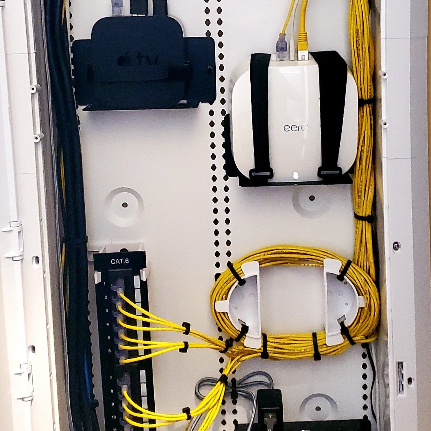 A white network cabinet with yellow and black cables, housing a router and other networking hardware.