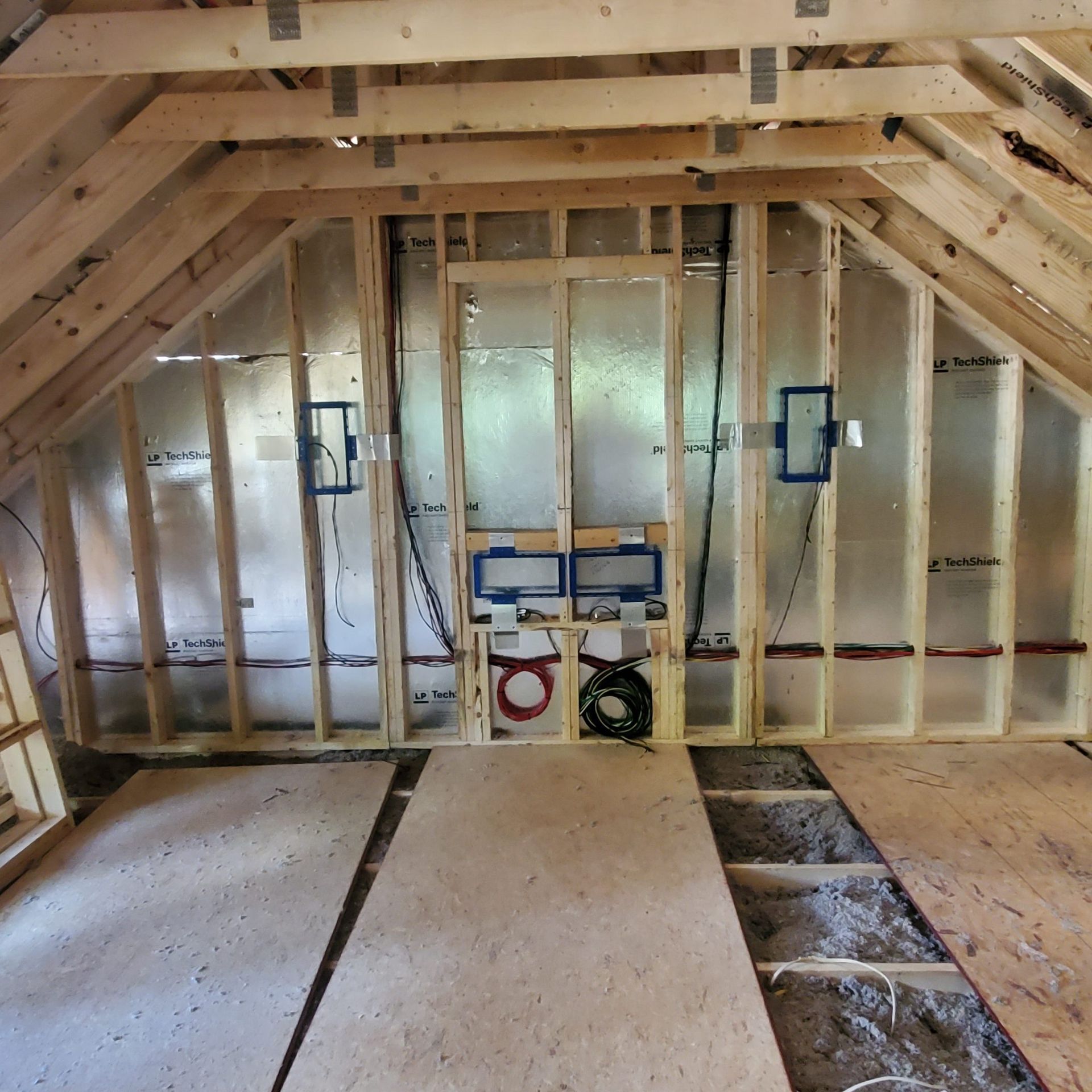 Interior view of a room under construction. Wooden frame with insulation, electrical boxes, plumbing, and unfinished floor.