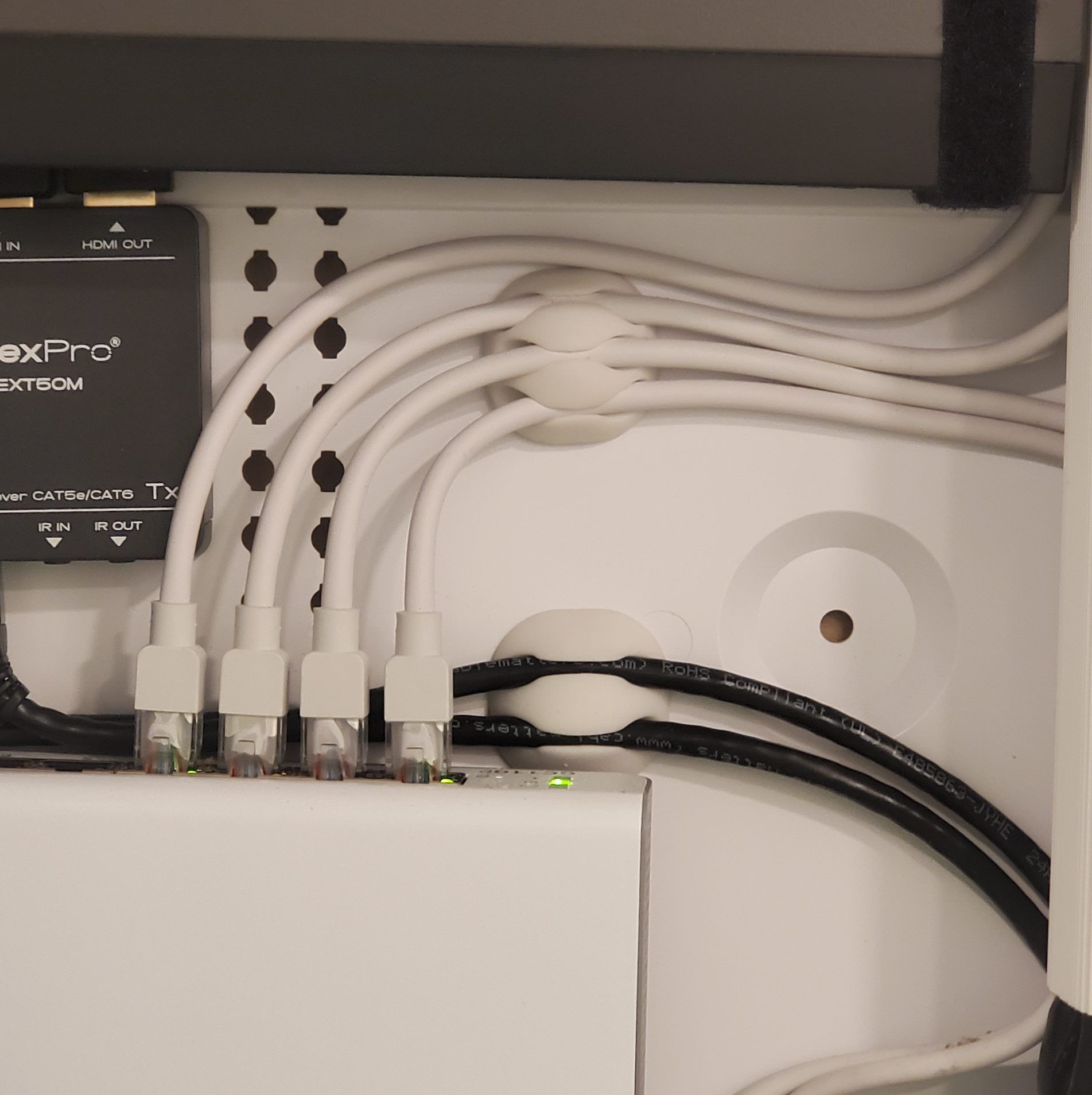 White and black cables are organized through a white panel. Ethernet cables are plugged into a switch.