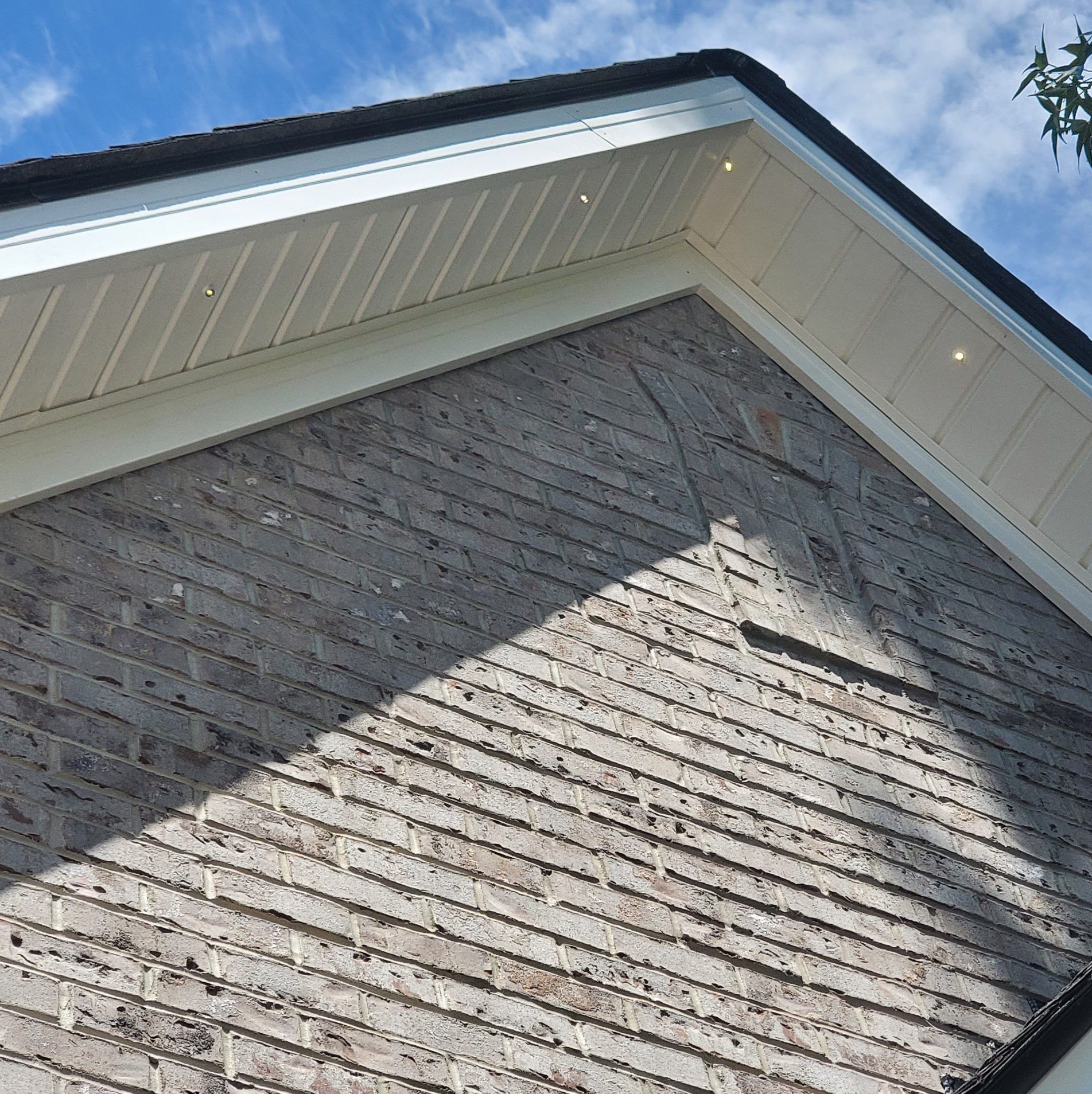 Close-up of a brick exterior of a house with white soffit and facia with integrated lights, against a blue sky.