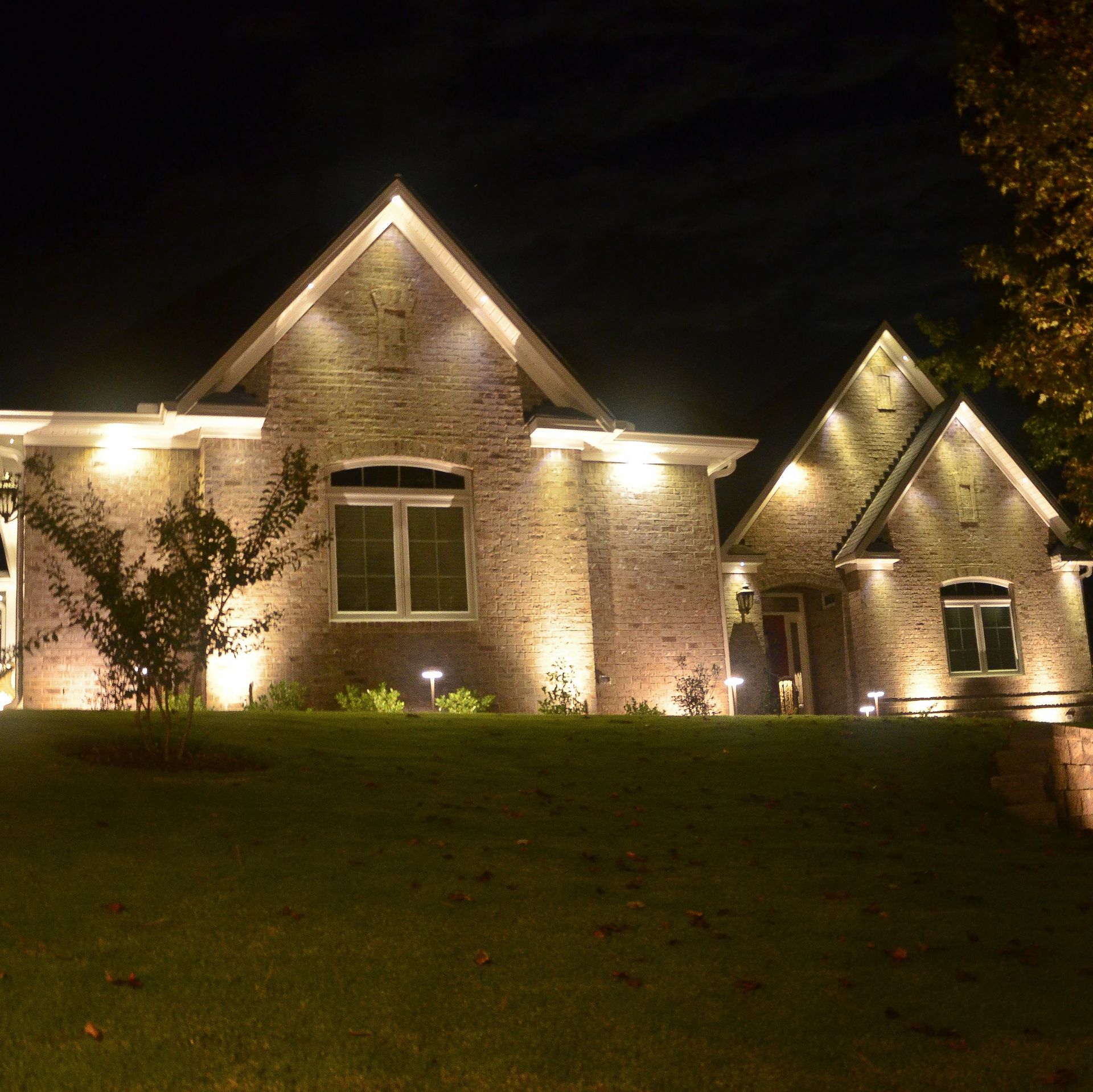 A brick house illuminated at night with up-lighting and pathway lights, highlighting the architecture. 
