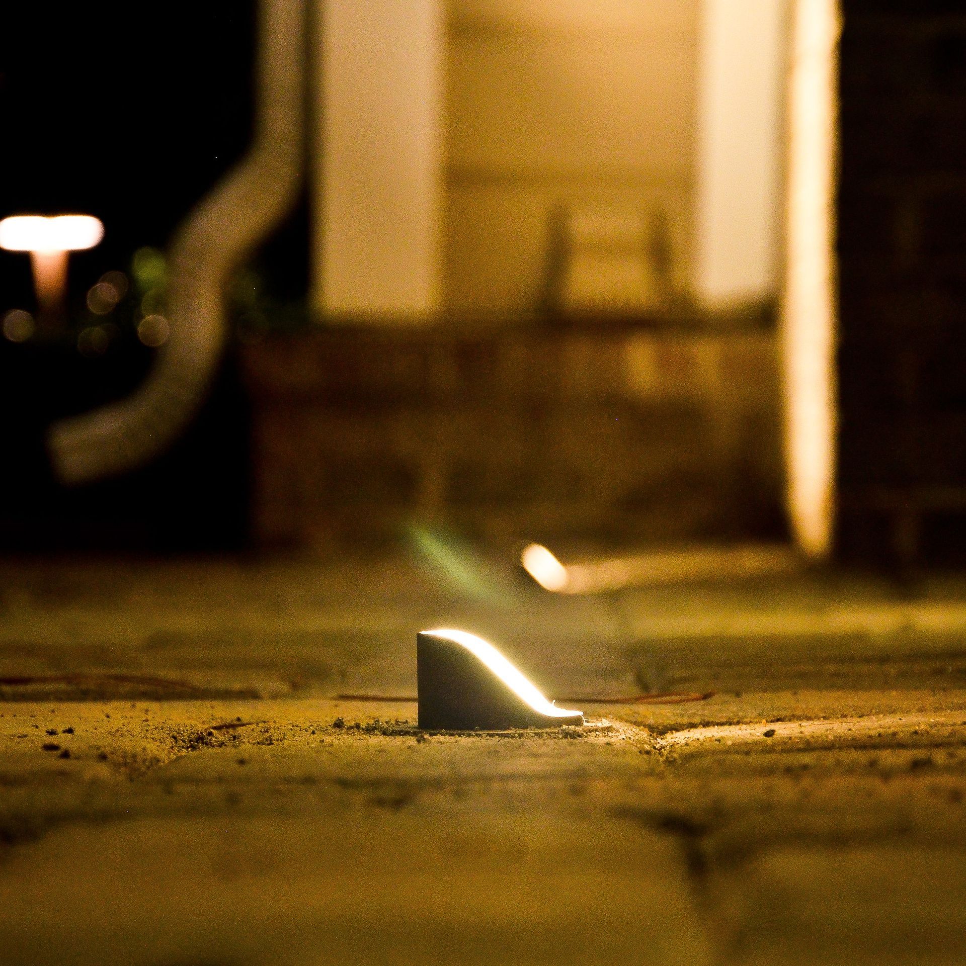 A low-angle, nighttime shot of a small, angled outdoor light illuminating a textured surface. The background is out of focus.