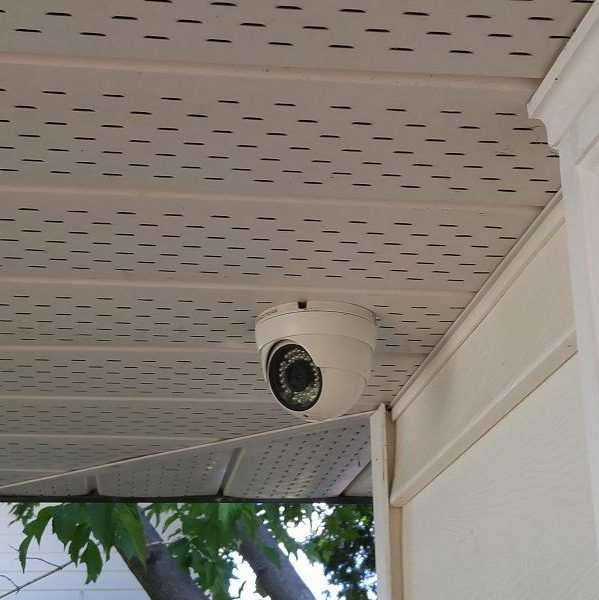 Security camera mounted on a cream-colored soffit, near the corner of a building.