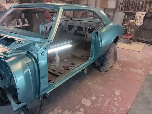 A teal-painted car body frame sitting on jack stands inside a garage workshop.