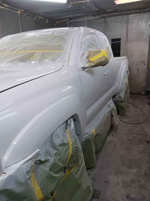 A white pickup truck masked with tape and plastic sheeting in an automotive spray booth.